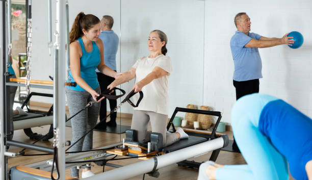 Elderly woman exercising on reformer with female pilates trainer stock photo