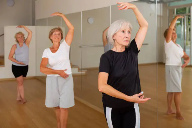 Photo of Mature woman practicing classic dance moves during group class