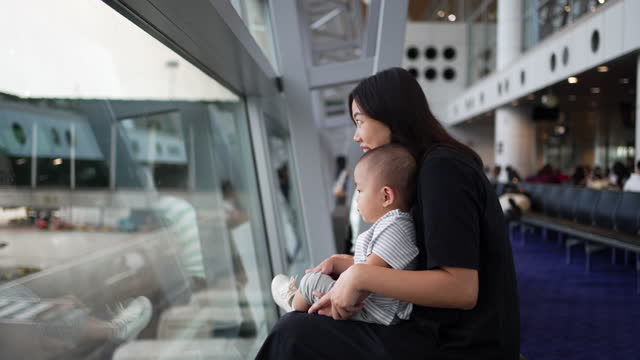 Mother and baby looking out window for airplane at airport