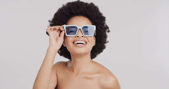 Sunglasses, black woman and portrait of a model in a white background studio with happiness. Smile, happy young person and natural afro of a female laughing with blue eyewear and a beautiful smile