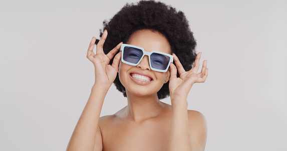 Black woman, studio portrait and sunglasses with smile, fashion or trendy style by gray background. African gen z model, happiness or beauty with summer accessory for safety from uv light in sunshine
