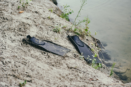 Black old flippers from the times of the USSR on the sand by the river, close-up photo