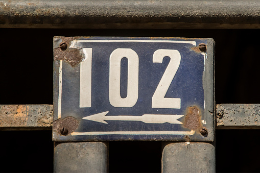 Weathered grunge square metal enameled plate of number of street address with number 102
