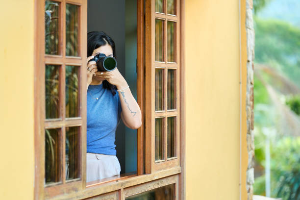 młoda fotografka robiąca zdjęcia z okna domu wakacyjnego - looking through window lens tourist image zdjęcia i obrazy z banku zdjęć