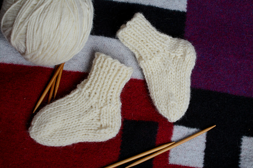 Blue knitted woolen scarf and mittens and knitting needles on a white background, homemade needlework concept, top view