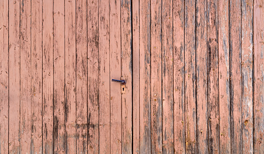 Old double wing wooden garage door with heavily weathered paint and doorknob