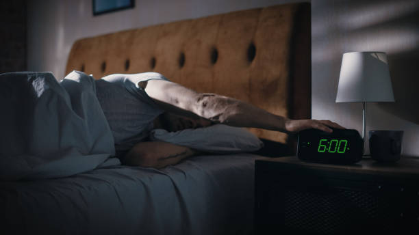 Man Wakes Up, Turns off Alarm Clock with Frustration, after Sleepless Insomniac Night. Early Rising Stressed Man Ready to Face Day of Problem Solving. Focus on the Clock Showing Six A.M. el hombre se despierta, apaga el despertador con frustración, después de una noche de insomnio sin dormir. hombre estresado de early rising listo para enfrentar el día de la resolución de problemas. concéntrese en el reloj que muestra las seis de la m