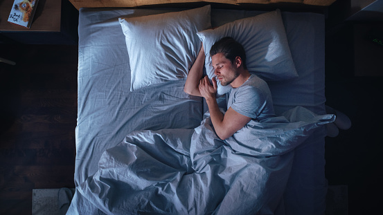 Top View Apartment Bedroom: Handsome Young Man Sleeping Cozily on a Bed in His Bedroom at Night. Comfortable Apartment with Guy Resting for Productive next Day. Top Down Above