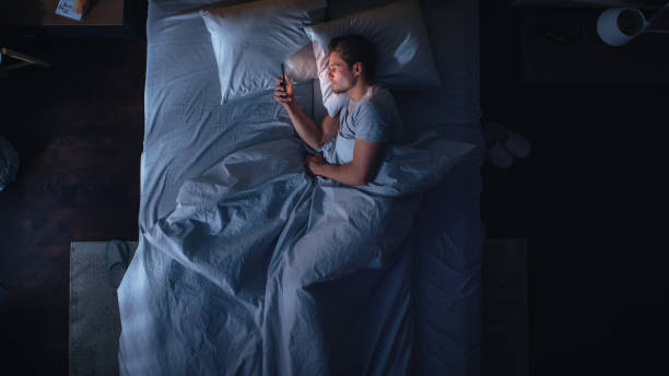 istock Top View Apartment Bedroom: Handsome Young Man Using Smartphone in Bed at Night. Guy Browsing Through Social Media, Using Dating Apps, Remote Work Software, Internet Online Shopping on Mobile Phone 1479313001