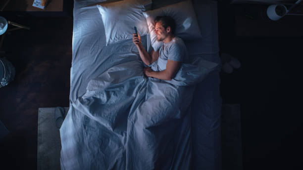 istock Top View Apartment Bedroom: Handsome Young Man Using Smartphone in Bed at Night. Smiling Guy Browsing Social Media, Dating Apps, Doing Internet Online Shopping on Mobile Phone. Top Down 1479313027