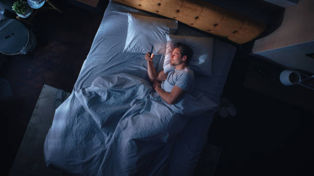 istock Top View Apartment Bedroom: Handsome Young Man Using Smartphone in Bed at Night. Smiling Guy Browsing Social Media, Dating Apps, Remote Work Software, Doing Internet Online Shopping on Mobile Phone 1479313108