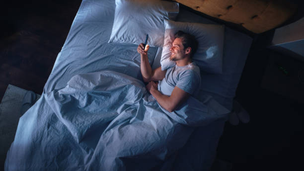 istock Top View Apartment Bedroom: Handsome Young Man Using Smartphone in Bed at Night. Smiling Guy Browsing Social Media, Dating Apps, Remote Work Software, Doing Internet Online Shopping on Mobile Phone 1479313150