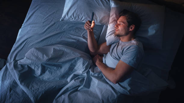 istock Top View Apartment Bedroom: Handsome Young Man Using Smartphone in Bed at Night. Smiling Guy Browsing Social Media, Dating Apps, Remote Work Software, Doing Internet Online Shopping on Mobile Phone 1479313186