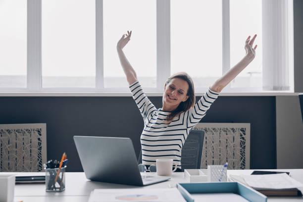istock Relaxed young woman stretching out hands and smiling while sitting at her working place 1479314023