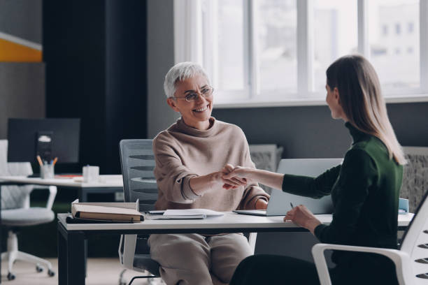 istock Two confident women shaking hands and smiling while sitting at the office desk together 1479314454