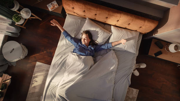 Top View Home: Beautiful Young Woman Sleeps in Her Bed, Sun Shines on Her and She Opens Eyes and Greets New Sunny Day. Joyful Waking Up of a Girl Ready for Productive Day. Top Down Above Shot