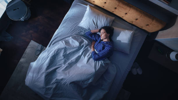 Top View of Beautiful Young Woman Sleeping Cozily on a Bed in Her Bedroom at Night. Comfortable Apartment with Sweet Girl Resting when Moonlight Shining Through Apartment Window. Top Down Top View of Beautiful Young Woman Sleeping Cozily on a Bed in Her Bedroom at Night. Comfortable Apartment with Sweet Girl Resting when Moonlight Shining Through Apartment Window. Top Down only women women bedroom bed stock pictures, royalty-free photos & images