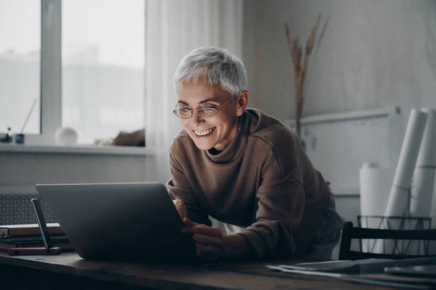 istock Confident senior woman using laptop and smiling while working late at home 1479316616
