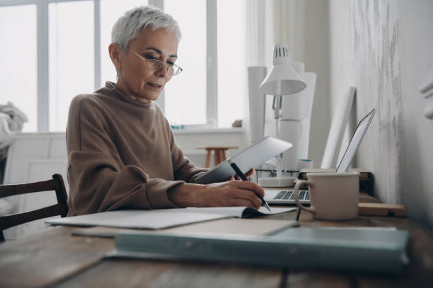 istock Concentrated senior woman making notes in pad while sitting at the desk in office 1479316754