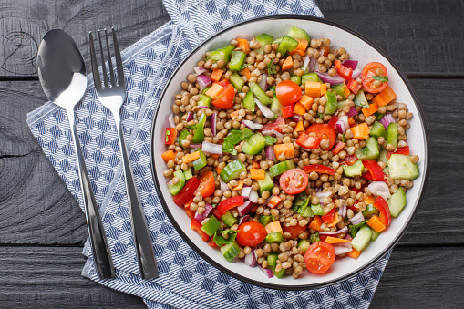 Vegetable salad with boiled lentils seasoned with olive oil close-up in a plate on a wooden table. Horizontal top view from above