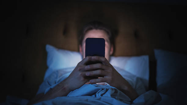 Anonymous Man Uses Smartphone in Bed at Home at Night. Handsome Guy Browsing Social Media, Reading News, Doing Online Shopping Late at Night. Focus on Hand Holding Mobile Phone Covering Face Anonymous Man Uses Smartphone in Bed at Home at Night. Handsome Guy Browsing Social Media, Reading News, Doing Online Shopping Late at Night. Focus on Hand Holding Mobile Phone Covering Face Phone Addiction stock pictures, royalty-free photos & images