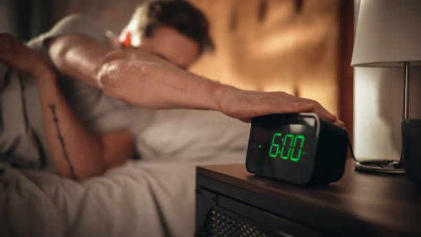 Man Wakes Up and Turns off Alarm Clock. Early Rising Productive Man Ready Start a Day full of New Business Projects, Adventures. Focus on Clock Showing Six O'Clock. Sun is Shining. bedroom Apartment el hombre se despierta y apaga el despertador. hombre productivo de early rising listo comience un día lleno de nuevos proyectos de negocios, aventuras. concéntrese en el reloj que muestra las seis en punto. el sol brilla. apartamento dormitorio