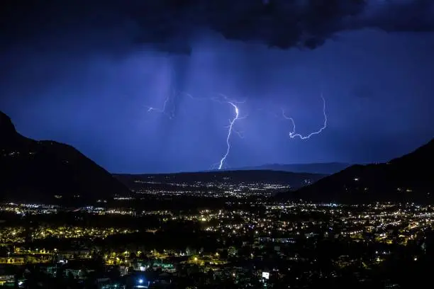 A lightning storm illuminating the night sky above a metropolitan area with a distant mountain range in the background
