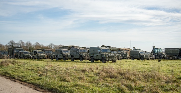 A cluster of military vehicles parked in a large grassy field, positioned in a neat row