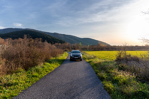 A gray car drives along a road in a green field in the spring mountains