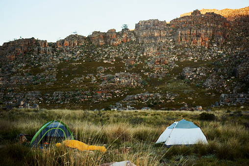 Camping, no people and nature landscape with a outdoor tent and gear to go camp. Mountains, grass field and blue sky with tents for vacation and travel experience outside in summer for vacation