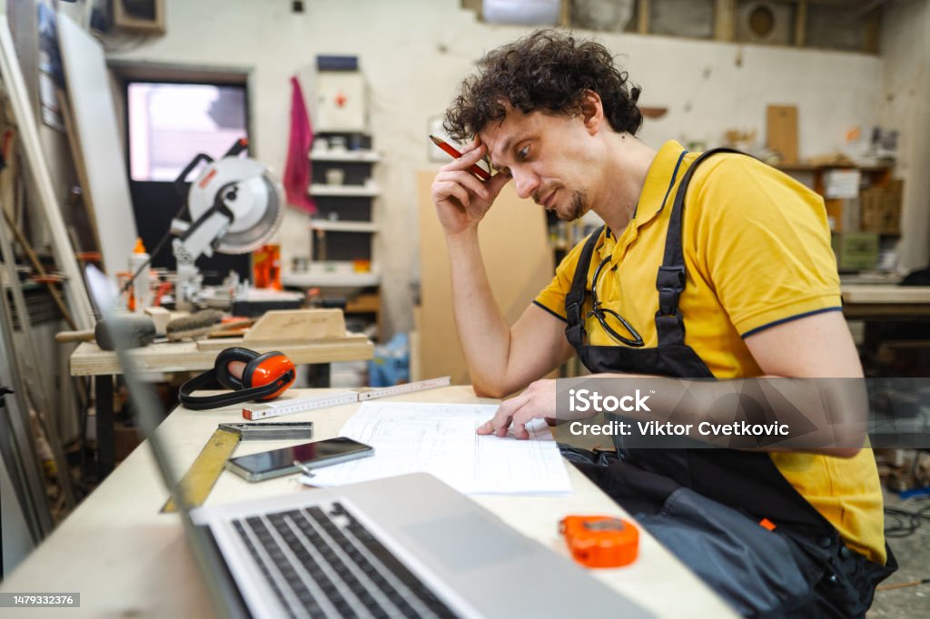 Worried craftsman working on blueprint at the woodshop Laptop Stock Photo