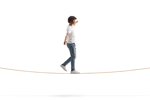 Full length profile shot of a young african american man walking on a tightrope and keeping balance isolated on white background