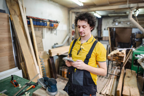 istock Carpenter using mobile phone while on a mini break from working at the woodshop 1479332683