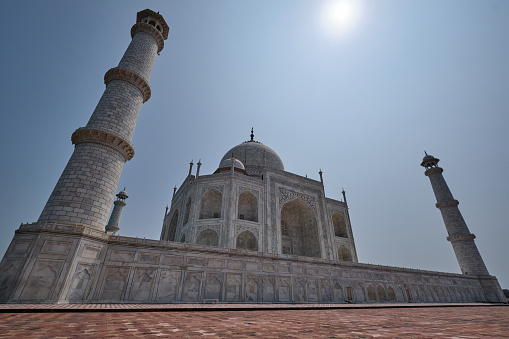 Taj Mahal from its right side with the afternoon sun overhanging high up in the clear blue sky. No humans in the photo