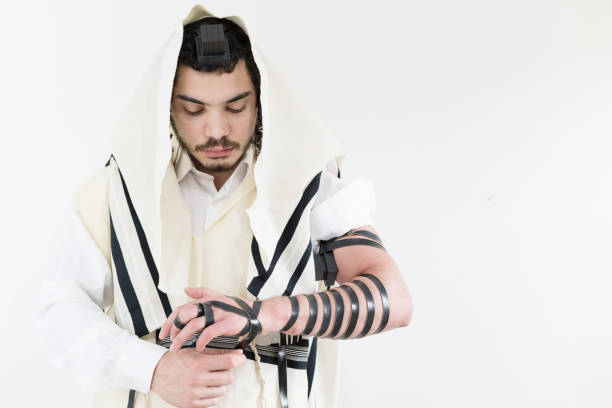 giovane ebreo ortodosso in scialle (tallit) che mette su filatteri (tefillin) sul braccio sinistro - phylactery foto e immagini stock