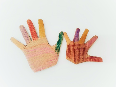 The form of hands made out of cardboard of an adult and a child, painted with colored pencils by a child as a school homework.