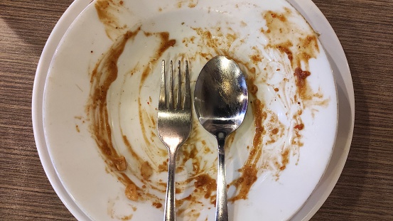Dirty white plate with silver spoon and fork on it because of peanut sauce.