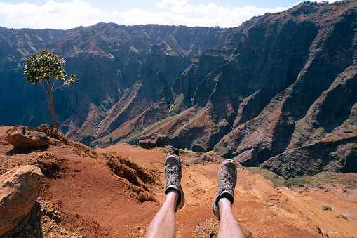 Man's feet hanging over cliff on Waipo'o falls via Pu'u Hinahhina and canyon trail Koke'e State park Kauai Hawaii USA