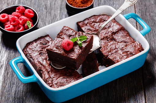 chocolate brownies with fresh raspberry and mint in a blue baking dish on dark wood table, close-up