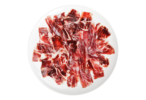 Slices of ham cutted by hand on a white plate over a white background