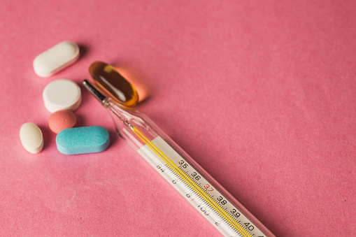 A closeup of medical pills and a thermometer on a pink surface