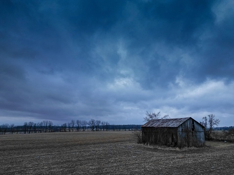 A solitary shed in an open field surrounded by an ominous in Indiana