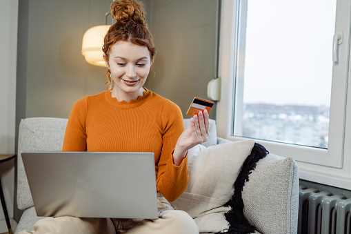 Young woman holding a credit card. She is doing an online shopping on the laptop.
