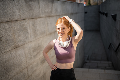 Sportswoman running outdoors, young red-haired sports active woman running next to a concrete wall
