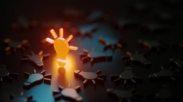 Orange Light Bulb Symbol Glowing Amid Black Lightbulb Symbols On Black Background