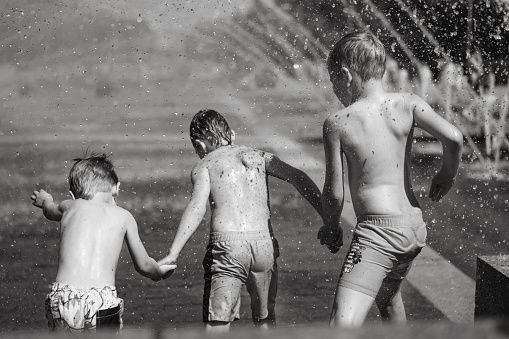 Three caucasian boys going to run throgh splashing fountain on hot summer day in city of Saint-petersburg, Russia. High quality photo