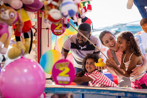 A family enjoying a day out at the fair in Newcastle upon Tyne, North East England. They are playing hook-a-duck together and the mother is congratulating her daughter after successfully catching a duck to win a prize.