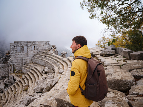 Autumn walk , man in yellow jacket looks at the ancient amphitheatre in city Termessos Ancient City, Turkey. Turkeys most outstanding archaeological sites and one of main tourist center.