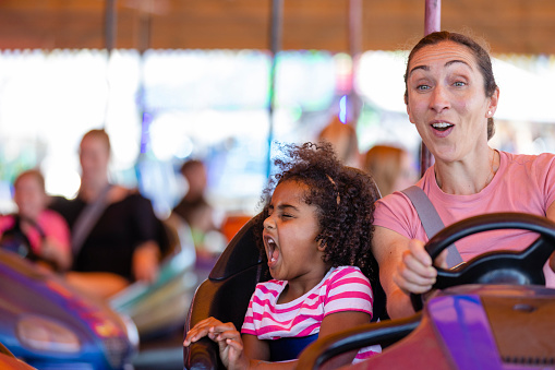 Cute little girls with their mother and father enjoying ride at fun fair, young family, amusement park