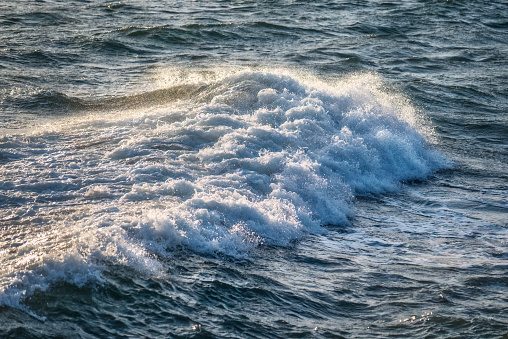 Close up detail of powerful teal blue wave breaking in open ocean on a bright sunny afternoon